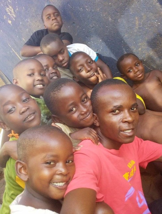 Bugingo, in a pink T-shirt, taking a selfie with ten smiling Desire Kids crowded around and behind him.
